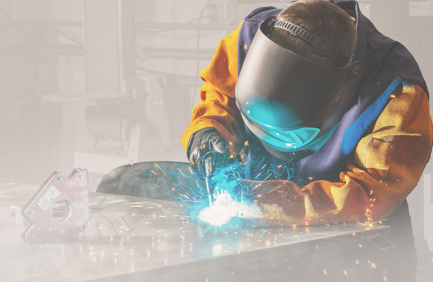 A person in a yellow jacket and helmet who is welding with sparks coming off.