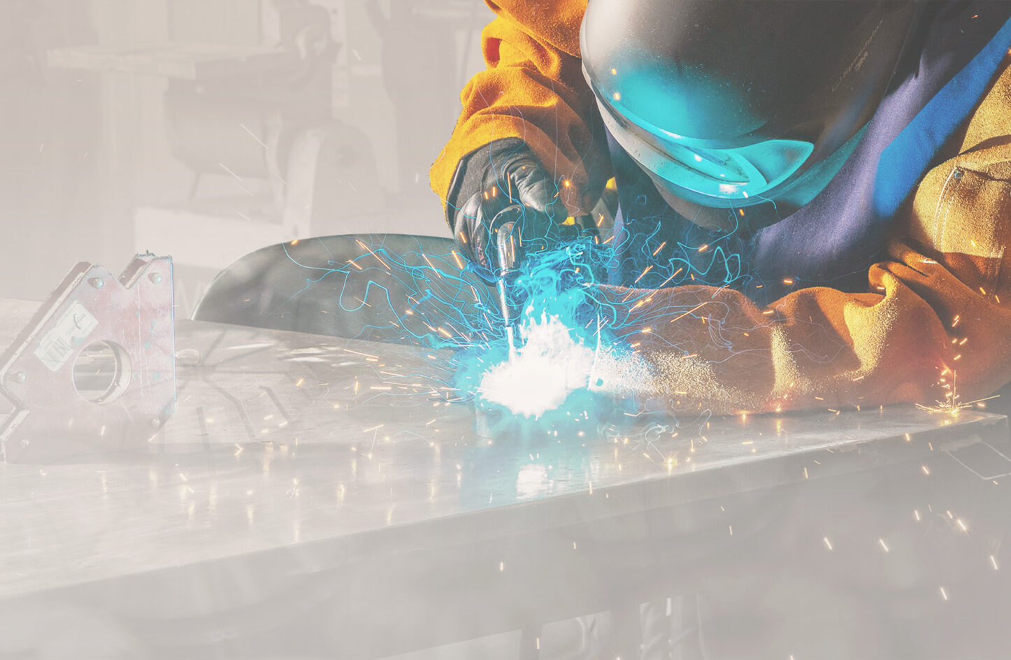 A person in a yellow jacket and helmet who is welding with sparks coming off.