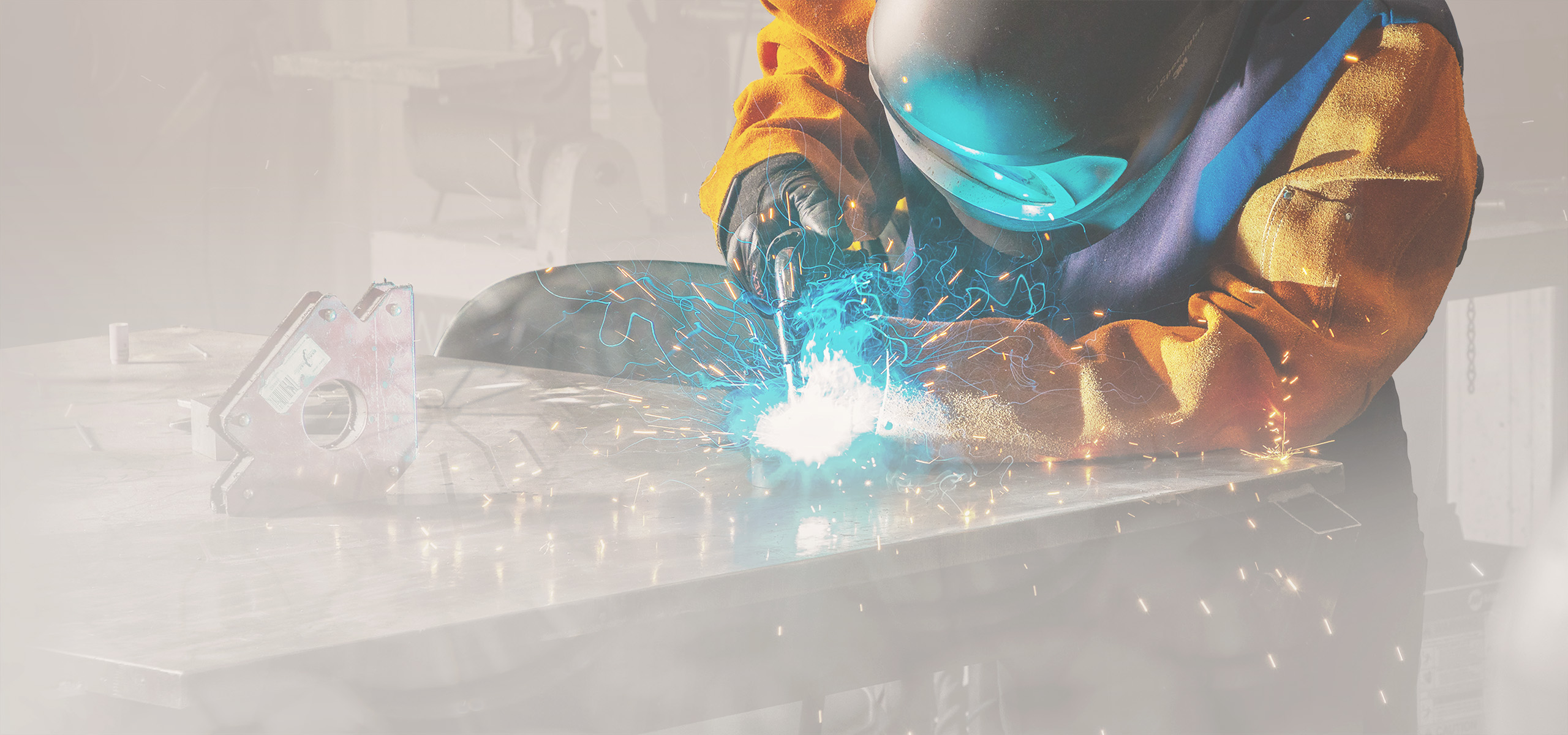A person in a yellow jacket and helmet who is welding with sparks coming off.