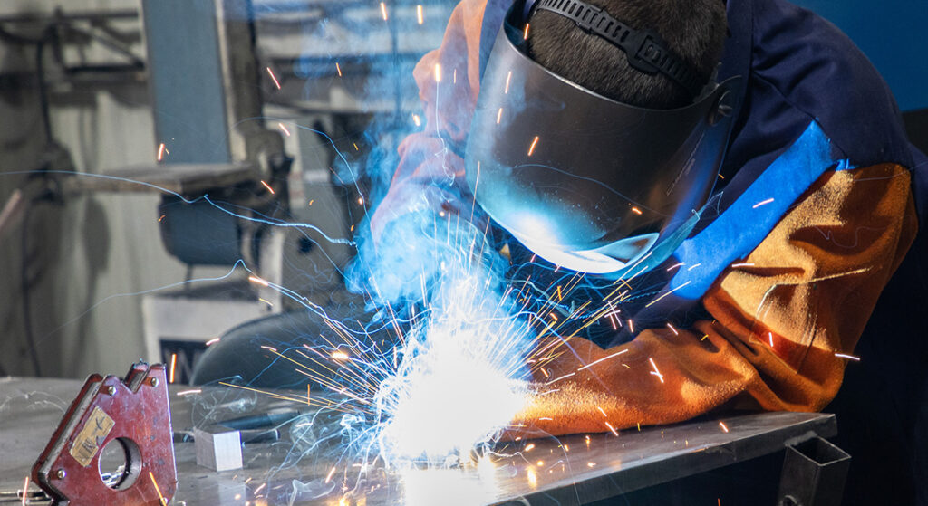 A person in a yellow jacket and helmet who is welding with sparks coming off.