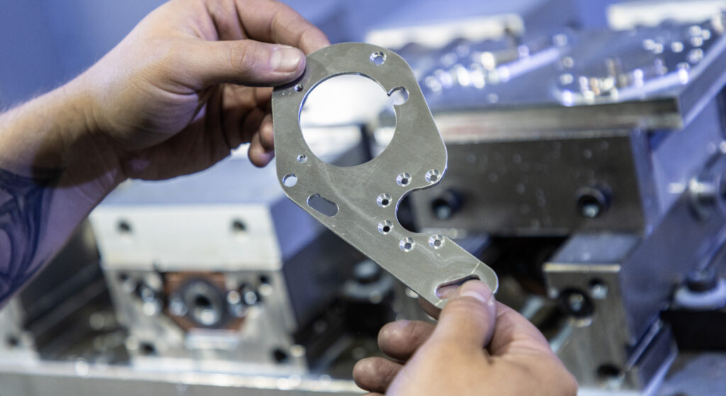 A person holding a shiny silver machined part in their hands.
